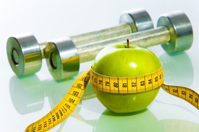 apple with measuring tape and weights, as symbols of weight loss