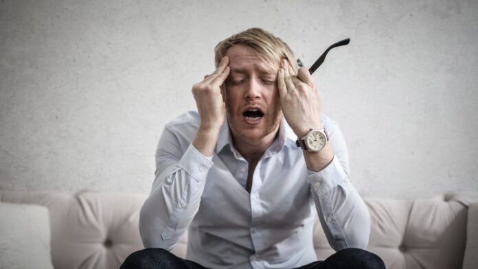 Photo of a seated man with his fingers on his temples, and an anxious expression on his face.