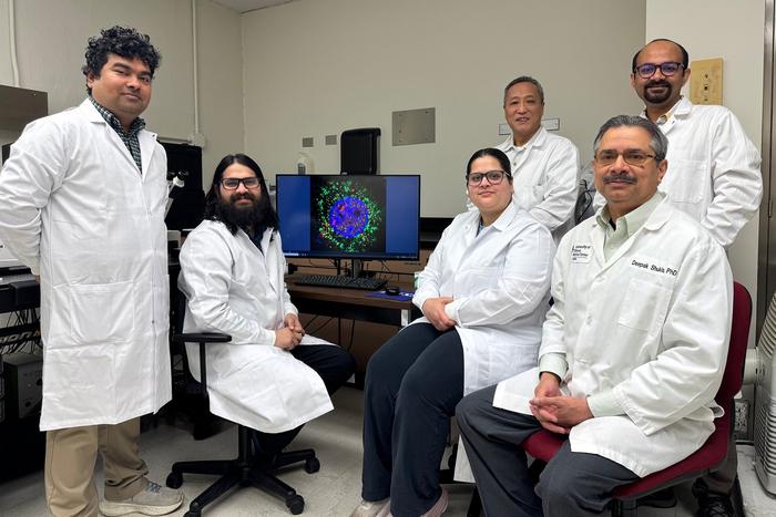Group photo of Deepak Shukla's team who discovered that doxorubicin fights herpes posing with a confocal microscopy image of a cell.